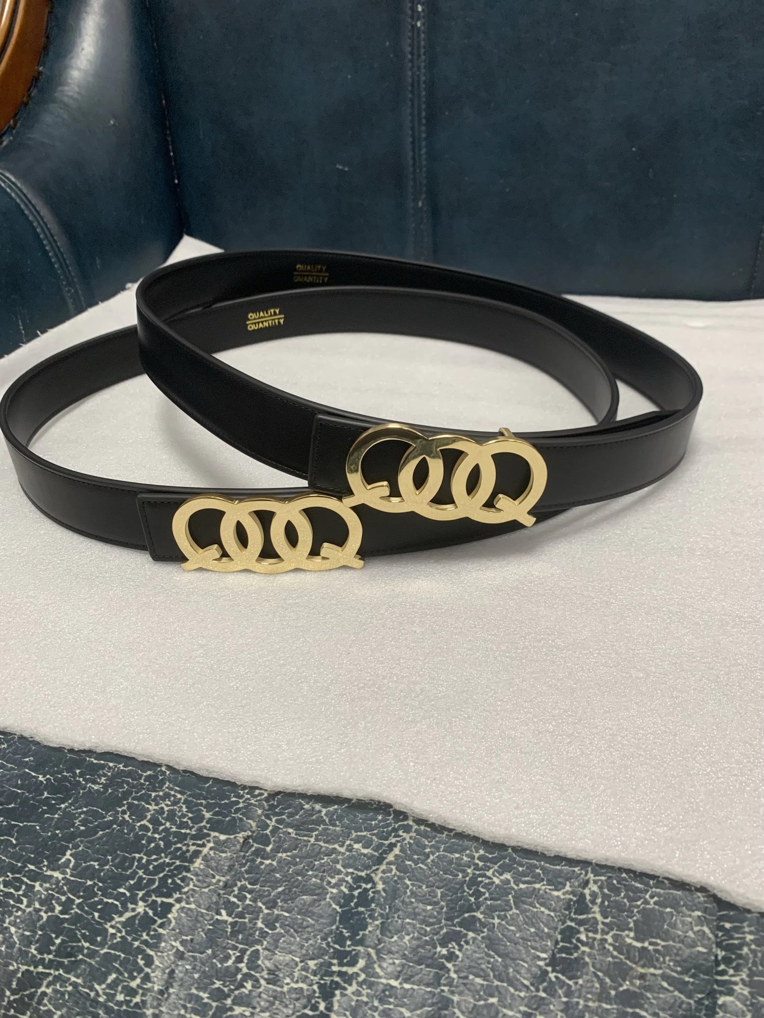 Black belt with gold QOQ buckle on a white surface